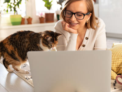 Woman smiling at cat, both sitting in front of laptop